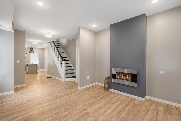 Open living room with plank floors, recessed lights and an electric fireplace in a gray accent wall