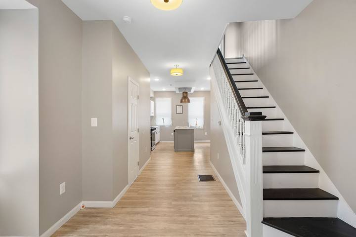Front hall with a white staircase, dark stair treads and plank floors running back to the kitchen