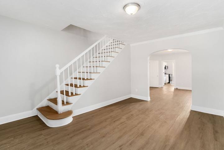 Living room with a white staircase and an arched doorway to the dining room
