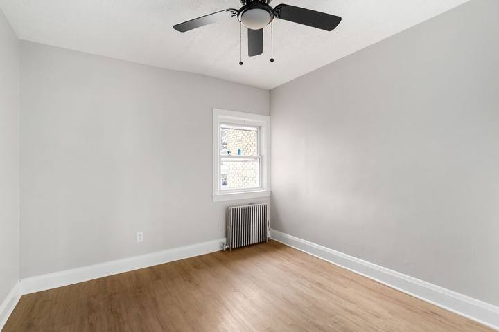Bedroom with plank floors, a ceiling fan and a radiator under the window