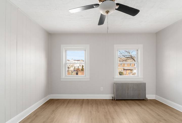 Bedroom with two windows, a ceiling fan and paneled walls