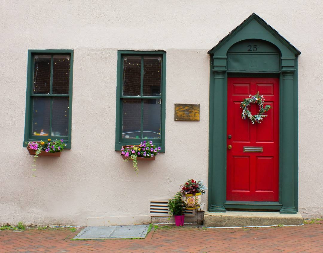 Red front door with a wreath, green-trimmed windows and flower boxes on a historic house in Annapolis