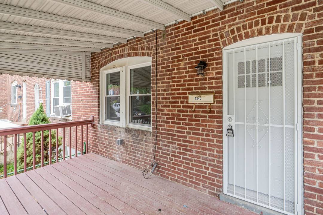 Covered front porch and white security door of a brick rental townhouse on Pontiac Avenue in Baltimore